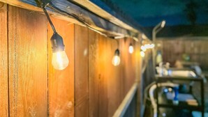 A row of hanging light bulbs against a wooden wall. - Urban Glamping Oasis: Comfort & Adventure Combined (Glendora)