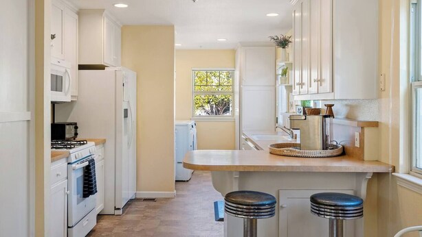 Une cuisine avec des meubles blancs, une cuisinière, un four à micro-ondes et une fenêtre donnant sur les arbres.