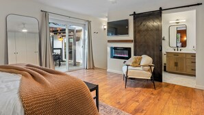 Un dormitorio moderno con una cama grande, una silla, una chimenea y una puerta corrediza que da a un balcón.