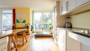 A modern kitchen with wooden flooring, a dining area with a table and chairs, and a large window offering a view of greenery. - Spacious 3-bedroom with 3 balconies, 2 bthrms, sea view and free indoor parking (Oslo)