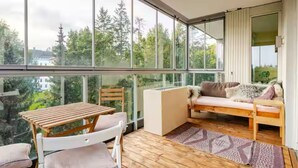A modern room with a wooden table and chairs, a sofa with cushions, and large windows offering a view of trees and buildings. - Spacious 3-bedroom with 3 balconies, 2 bthrms, sea view and free indoor parking (Oslo)