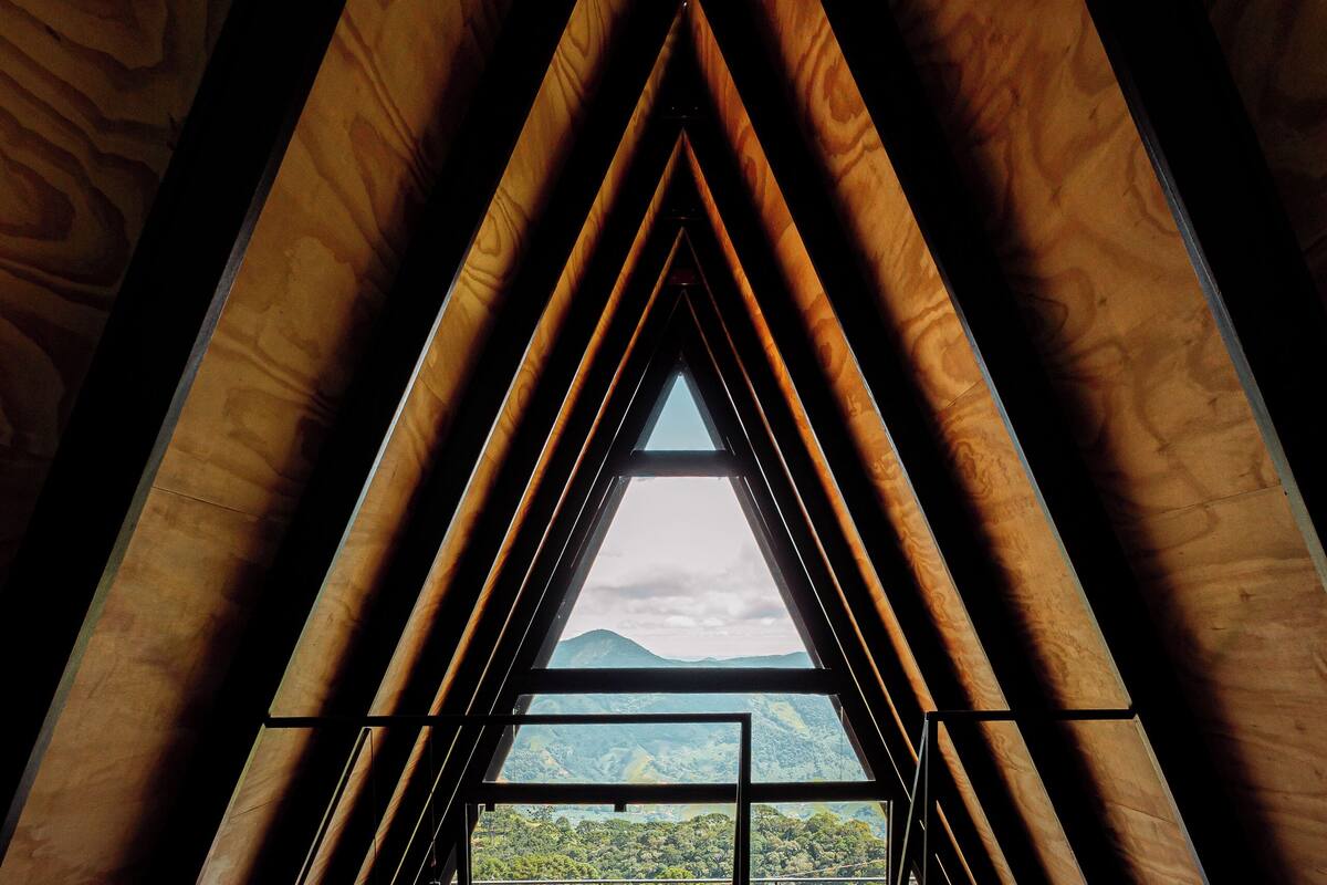 A triangular attic bedroom with a view of a mountainous landscape through a large window.