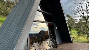 Un espacio exterior moderno y triangular con terraza de madera, dos sillas de metal y una mesa redonda.