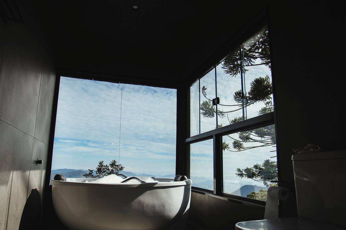 A modern bathroom with a freestanding bathtub, a toilet, and large windows offering a view of mountains and trees.