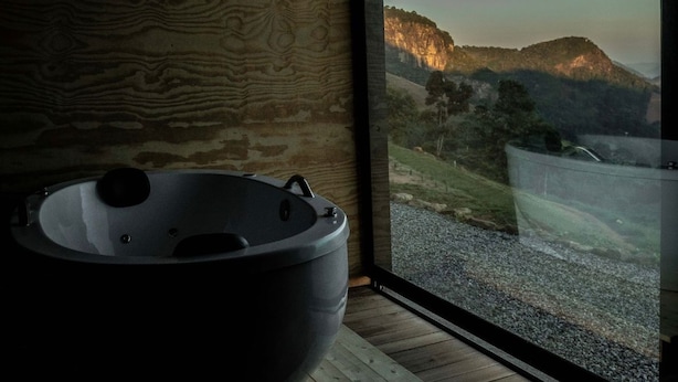 Un baño moderno con una bañera grande, paredes de madera y vistas a un paisaje montañoso.