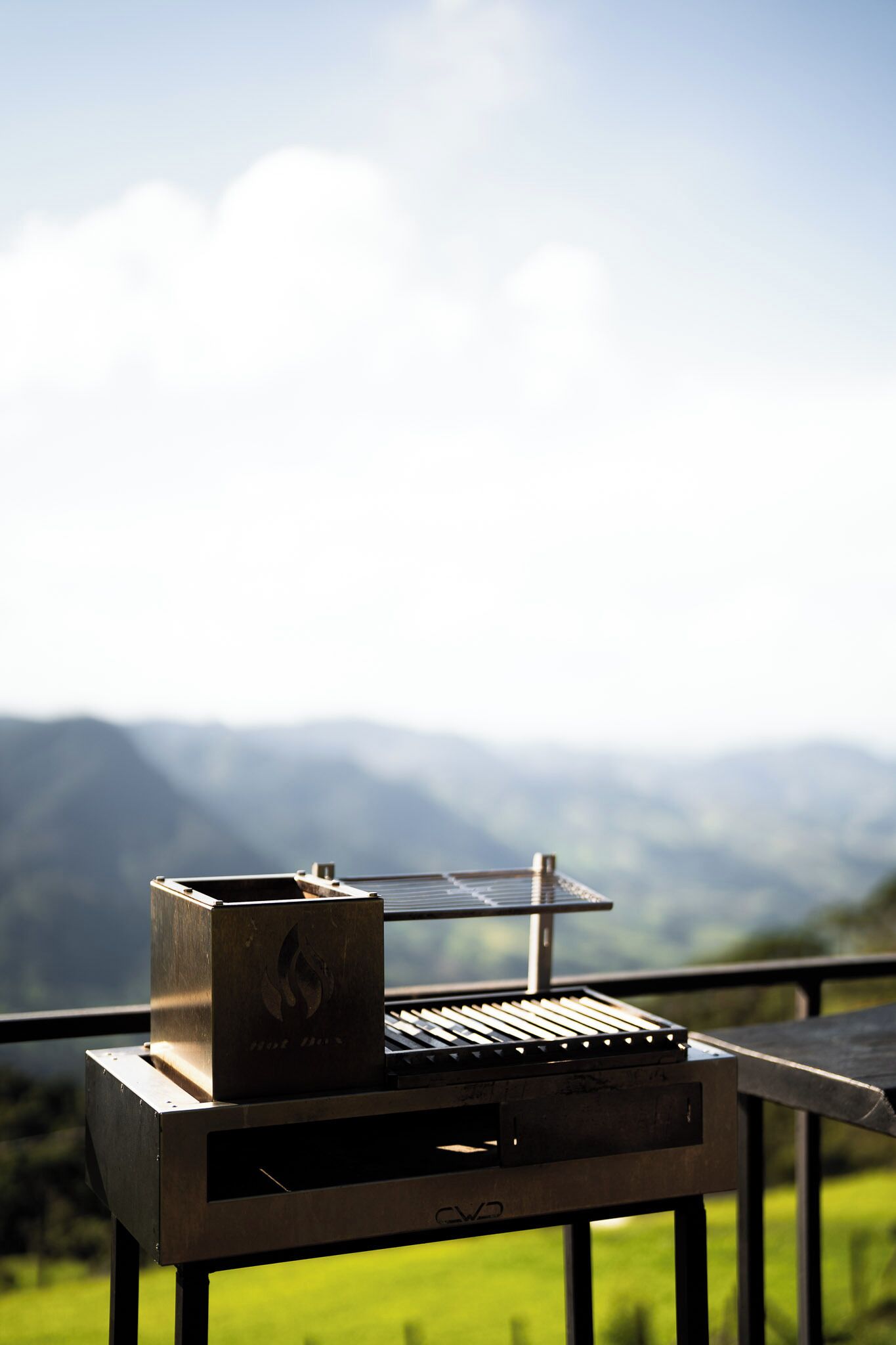 Ein tragbarer Grill auf einem Balkon mit Blick auf eine schöne Berglandschaft im Hintergrund.