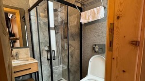 Un baño con ducha envuelta en vidrio, tocador de madera con lavamanos y un inodoro.