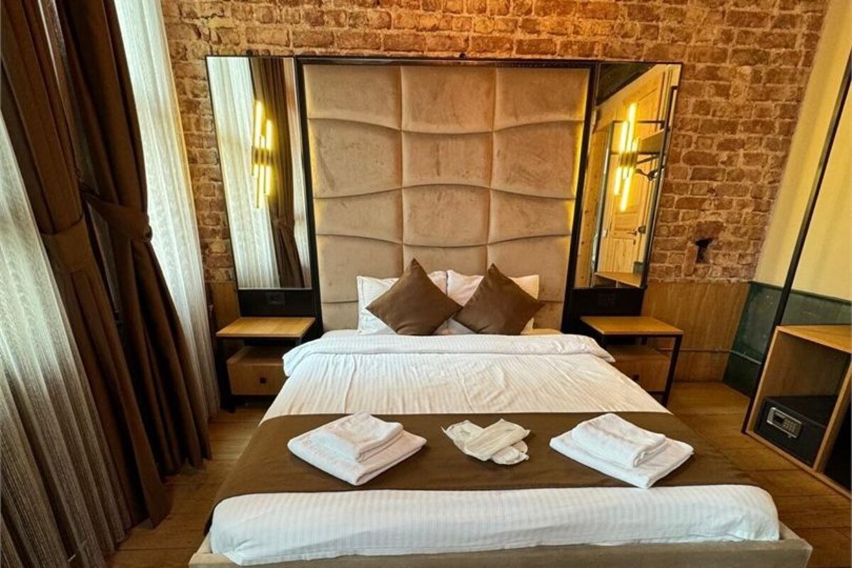 Un dormitorio con pared de ladrillo, cabecera capitonada, cama grande con almohadas, mesita de noche y espejo.