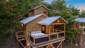 Una cabaña de madera con un jacuzzi en la terraza, rodeada de árboles.