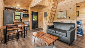 Interior acogedor de una cabaña con comedor, sofá y cocina, paredes de madera y puerta negra.