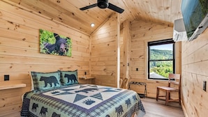A wooden cabin bedroom with a bed, a chair, a window with a view, and a ceiling fan. - TreeLodge, Downtown Pigeon Forge (Pigeon Forge)
