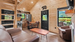 A log cabin interior with a dining area, kitchen, and a large window offering a view of the outdoors. - TreeLodge, Downtown Pigeon Forge (Pigeon Forge)