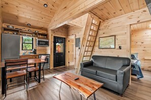 Interior de una cabaña de madera con comedor, sofá y cocina.