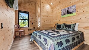 A wooden cabin bedroom with a bed, a chair, a window, and a bear-themed quilt. - TreeLodge, Downtown Pigeon Forge (Pigeon Forge)