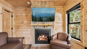 L’intérieur d’un chalet chaleureux, avec une cheminée, des murs en bois et deux canapés en cuir.