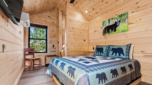 Une pièce de cabane en bois comprenant un lit, une chaise, une fenêtre et une courtepointe à motifs d’ours.