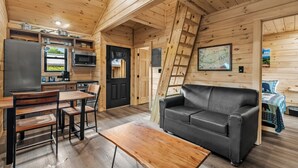 A wooden cabin interior with a dining area, a sofa, a kitchen with a refrigerator and stove, and a ladder. - TreeLodge, Downtown Pigeon Forge (Pigeon Forge)