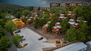 A resort with elevated wooden cabins, a central parking area, and a building with multiple floors in the background. - Little Forge TreeLodge, Downtown Pigeon Forge (Pigeon Forge)
