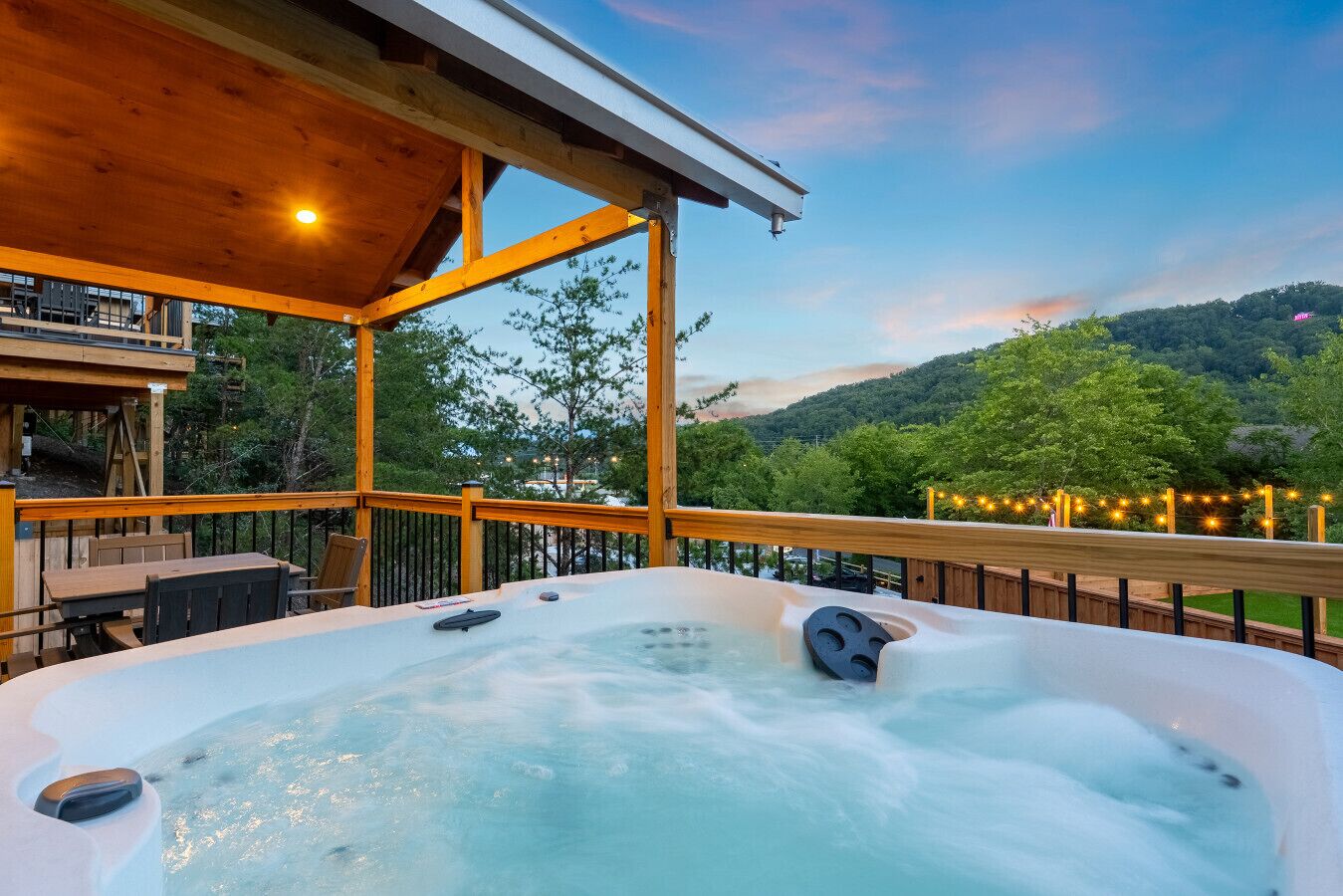 Een hottub op een houten terras, met uitzicht op een beboste heuvel.