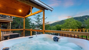 Un jacuzzi en una terraza de madera con vistas a una colina boscosa.