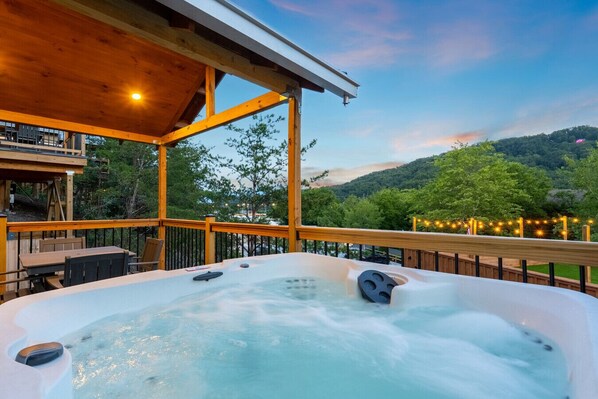 Un bain à remous sur une terrasse en bois, avec vue sur une colline boisée.