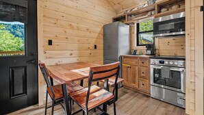 Un interior de madera con una mesa de comedor, sillas, un refrigerador, un horno y una ventana con vistas a la vegetación.