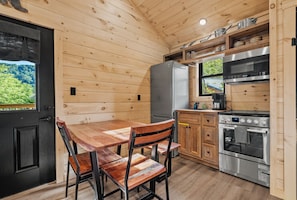 A wooden interior with a dining table, chairs, a refrigerator, an oven, and a window with a view of greenery. - TreeLodge, Downtown Pigeon Forge (Pigeon Forge)