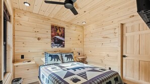 Une chambre dans une cabane en bois, avec un lit, un ventilateur de plafond, un tableau et une porte en bois.