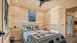 Et træhytteværelse med seng, ventilator, et billede og en dør til et badeværelse.