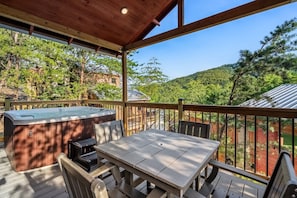 A covered outdoor deck with a hot tub, a table, and chairs.