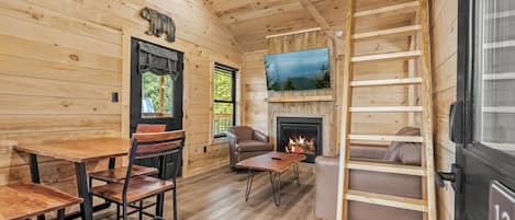 A cabin interior with a wooden interior, a fireplace, a television, and a dining area.