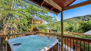 A hot tub on a wooden deck with a view of a forested area and a mountain in the background.