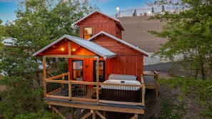 A wooden cabin with a deck, a hot tub, and a stone wall in the background. - TreeLodge, Downtown Pigeon Forge (Pigeon Forge)