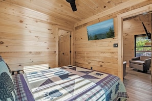 A wooden cabin interior with a bed, a painting, and a view of the outdoors. - TreeLodge, Downtown Pigeon Forge (Pigeon Forge)