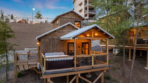 A wooden cabin with a hot tub, deck, and a stone wall in the background. - TreeLodge, Downtown Pigeon Forge (Pigeon Forge)