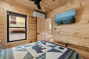 Een kamer met houten wanden, een bed met sprei, een raam met uitzicht en een airconditioning.