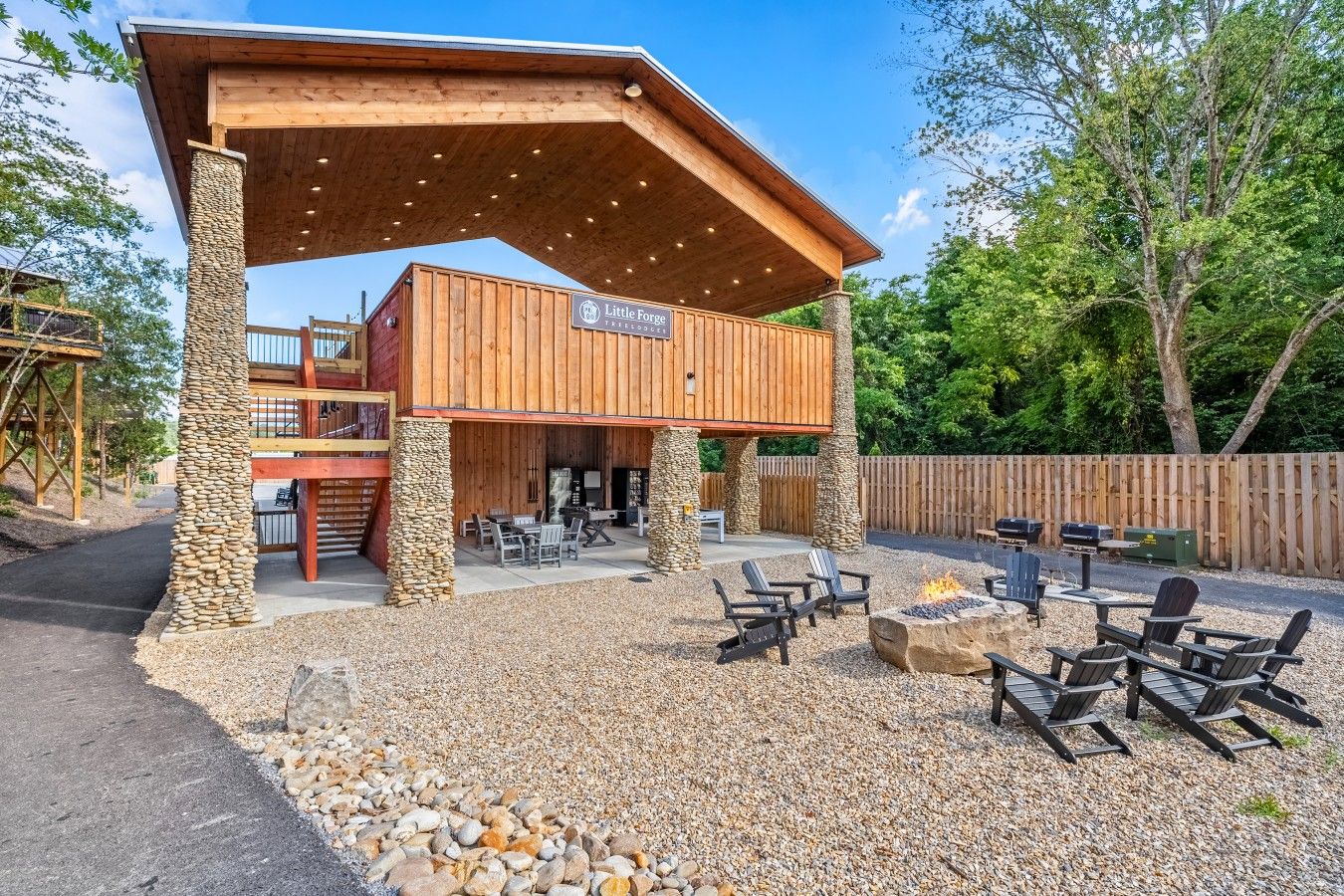 A rustic outdoor patio with a covered seating area, stone pillars, and a fire pit.
