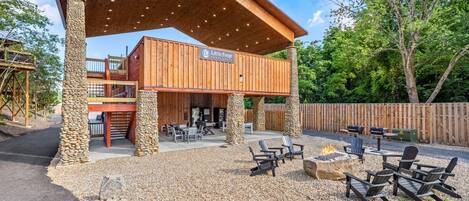 A rustic outdoor patio with a covered seating area, stone pillars, and a fire pit.