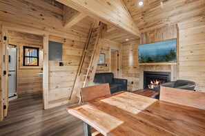 A wooden interior with a fireplace, a dining table, and a sofa. - TreeLodge, Downtown Pigeon Forge (Pigeon Forge)