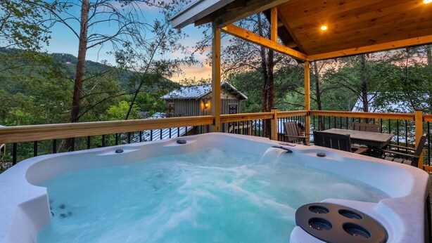 A hot tub on a wooden deck with a view of a cabin and trees.