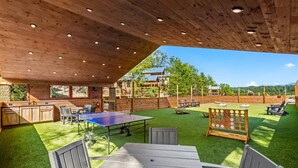 An outdoor area with a ping pong table, seating, and a wooden deck.