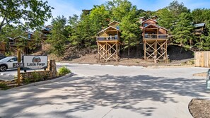 A residential area with two wooden houses on stilts, a sign for 'Little Forge Treehouses', and a paved driveway. - TreeLodge, Downtown Pigeon Forge (Pigeon Forge)