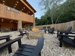 An outdoor seating area with Adirondack chairs, a stone fire pit, and a wooden building labeled 'Little Forge Treelodge.' - TreeLodge, Downtown Pigeon Forge (Pigeon Forge)