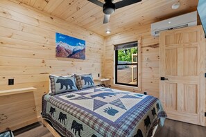 A wooden-paneled room with a bed, a window, and a door. - TreeLodge, Downtown Pigeon Forge (Pigeon Forge)