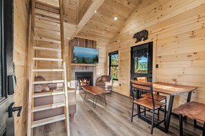 A cozy cabin interior with a fireplace, wooden walls, a TV mounted on the wall, and a dining area with benches. - TreeLodge, Downtown Pigeon Forge (Pigeon Forge)