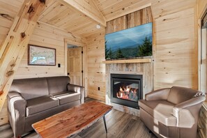 A cozy cabin interior with a fireplace, wooden walls, a sofa, and a coffee table. - TreeLodge, Downtown Pigeon Forge (Pigeon Forge)