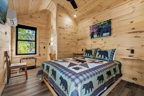 A wooden cabin bedroom with a bed, a chair, a window, and a bear-themed quilt.