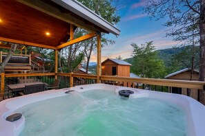 A hot tub with a wooden deck and a view of a cabin in the background.