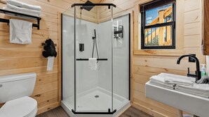 Een badkamer met houten lambrisering, een douchecabine met glazen wanden, een toilet en een wastafel met handdoeken.