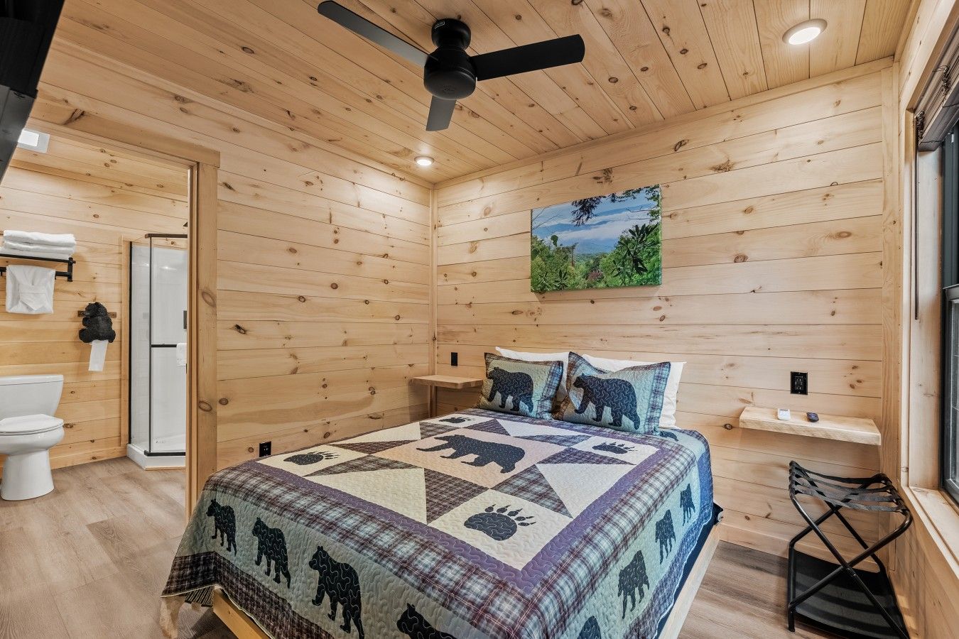 A wooden cabin bedroom with a bed, a ceiling fan, a shower, and a painting on the wall.
